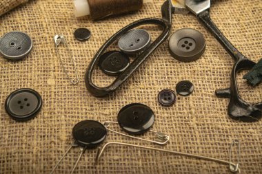 Çeşitli boyutlarda raptiyeler, terzi makası ve kalın desenli çuval bezi üzerindeki çeşitli düğmeler. Kapat.