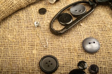 Çeşitli boyutlarda raptiyeler, terzi makası ve kalın desenli çuval bezi üzerindeki çeşitli düğmeler. Kapat.