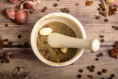 Seramik bir havanda baharat ve dağınık sarımsak karanfilleri, yıldız anason ve ahşap bir masanın üzerindeki tüm baharatlar. Kapat.