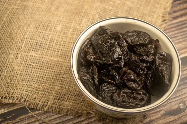 Dried prunes in a metal bowl on a wooden background. Close up