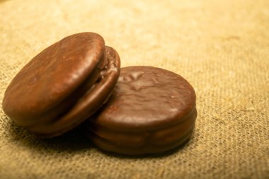 Ev yapımı kumaşın kabataslak desenli arka planında çikolatayla kaplı kurabiyeler. Kapat.