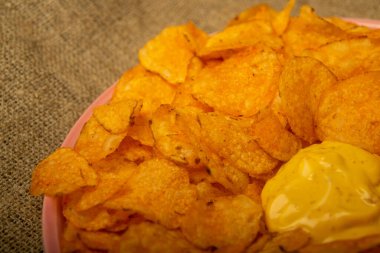 Yuvarlak tabakta patates cipsi ve peynir soslu tencere. Kapat.