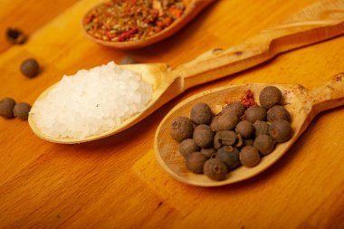 Kara baharat, kaba tuz ve ahşap bir tahtanın üzerinde tahta kaşıklardaki çeşitli baharatlar. Kapat.