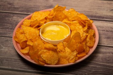 Yuvarlak tabakta patates cipsi ve peynir soslu tencere. Kapat.