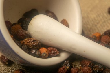 Seramik bir havanda kurumuş gül suyu meyvesi ve pürüzsüz bir deseni olan ev yapımı bir kumaşa saçılmış kuru gül ağacı meyvesi. Kapat.