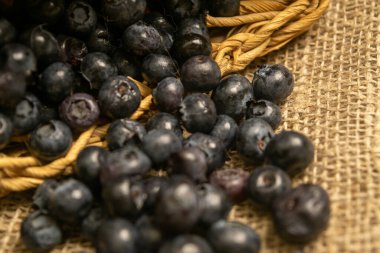 Hasır sepetteki yaban mersini ve yaban mersini kabataslak desenli ev yapımı kumaşın arka planına saçılmış. Kapat.