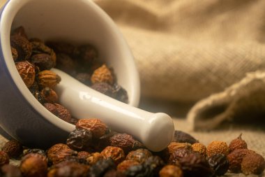 Seramik bir havanda kurumuş gül suyu meyvesi ve pürüzsüz bir deseni olan ev yapımı bir kumaşa saçılmış kuru gül ağacı meyvesi. Kapat.