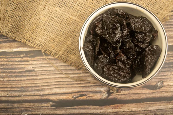 Dried prunes in a metal bowl on a wooden background. Close up