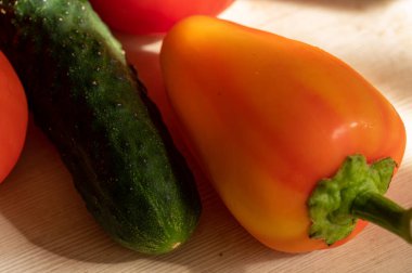 Olgun salatalık, sulu domatesler ve güneşte açık ahşap bir masada tatlı biberler. Kapat.