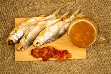 Kurutulmuş balık, kurutulmuş havyar ve tahta servis tahtasında bira kupası. Kapat.