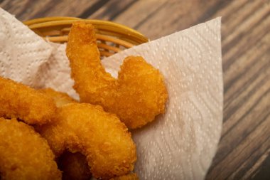 Hasır sepetteki beyaz kağıt peçetede hamurda kızartılmış Atlantik karidesleri. Kapat.