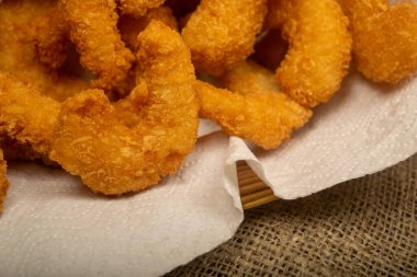 Hasır sepetteki beyaz kağıt peçetede hamurda kızartılmış Atlantik karidesleri. Kapat.