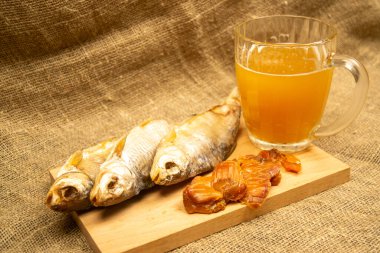 Kurutulmuş balık, kurutulmuş havyar ve tahta servis tahtasında bira kupası. Kapat.