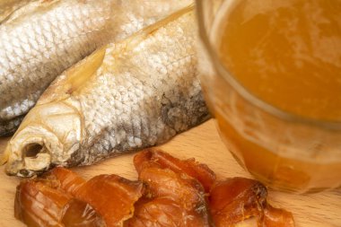 Kurutulmuş balık, kurutulmuş havyar ve tahta servis tahtasında bira kupası. Kapat.