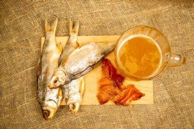 Kurutulmuş balık, kurutulmuş havyar ve tahta servis tahtasında bira kupası. Kapat.