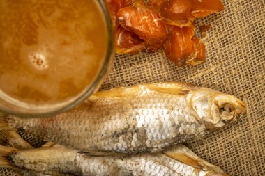 Kurutulmuş balık, kurutulmuş havyar ve kabataslak desenli ev yapımı kumaş üzerinde bira kupası. Kapat.