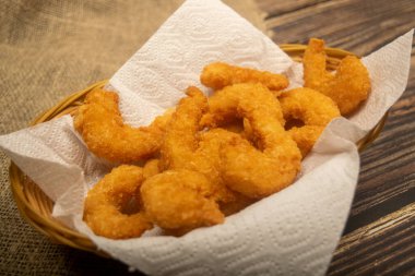 Hasır sepetteki beyaz kağıt peçetede hamurda kızartılmış Atlantik karidesleri. Kapat.