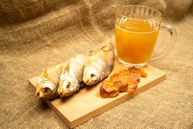 Kurutulmuş balık, kurutulmuş havyar ve tahta servis tahtasında bira kupası. Kapat.