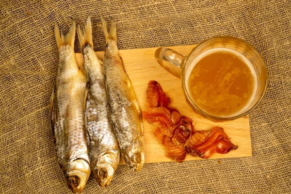 Kurutulmuş balık, kurutulmuş havyar ve tahta servis tahtasında bira kupası. Kapat.