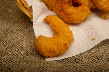 Hasır sepetteki beyaz kağıt peçetede hamurda kızartılmış Atlantik karidesleri. Kapat.