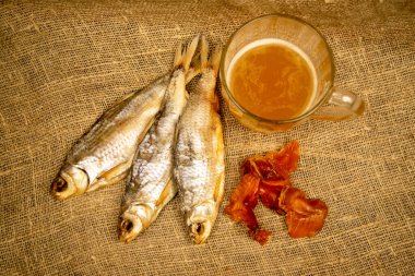 Kurutulmuş balık, kurutulmuş havyar ve kabataslak desenli ev yapımı kumaş üzerinde bira kupası. Kapat.