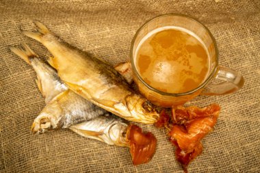 Kurutulmuş balık, kurutulmuş havyar ve kabataslak desenli ev yapımı kumaş üzerinde bira kupası. Kapat.