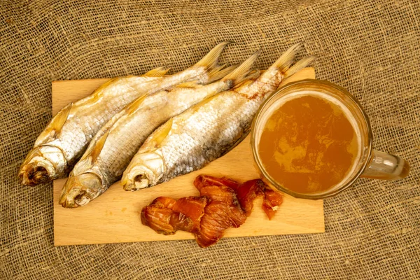 Kurutulmuş balık, kurutulmuş havyar ve tahta servis tahtasında bira kupası. Kapat.