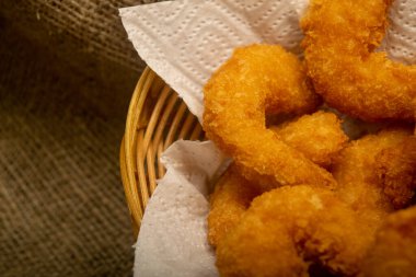 Hasır sepetteki beyaz kağıt peçetede hamurda kızartılmış Atlantik karidesleri. Kapat.