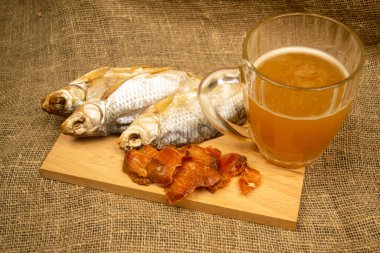 Kurutulmuş balık, kurutulmuş havyar ve tahta servis tahtasında bira kupası. Kapat.