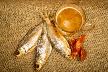 Kurutulmuş balık, kurutulmuş havyar ve kabataslak desenli ev yapımı kumaş üzerinde bira kupası. Kapat.