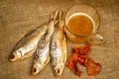 Kurutulmuş balık, kurutulmuş havyar ve kabataslak desenli ev yapımı kumaş üzerinde bira kupası. Kapat.