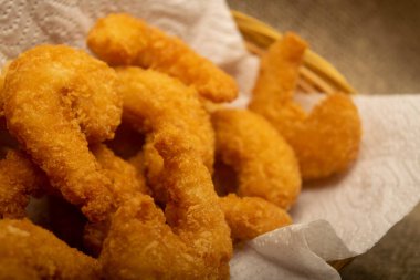 Hasır sepetteki beyaz kağıt peçetede hamurda kızartılmış Atlantik karidesleri. Kapat.