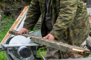 Bir adam dairesel testereyle eski bir soba tahtasını testereyle kesiyor, yakın plan, seçici odaklanma. Soba ısıtma, kırsal yaşam.