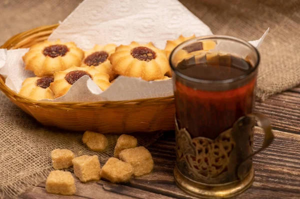 Homemade pastry cookies with jam and a faceted glass of tea in a vintage Cup holder on a background of homespun fabric with a rough texture, close-up, selective focus