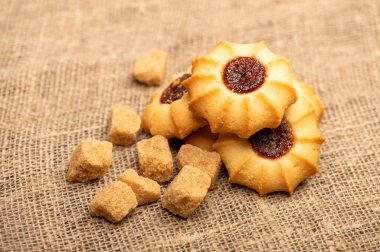 Ev yapımı hamur işi kurabiyeler reçelli ve kahverengi kamış şekerli ev yapımı kumaşın arka planında kaba bir desen, yakın plan, seçici odaklı.