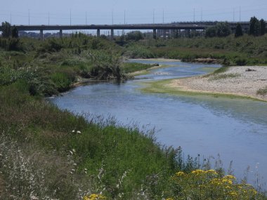 Rio baharda bir köprüyü geçerken, yansımaları ile mavi su gökyüzünün yansıması nedeniyle. Llobregat Nehri, Sant Feliu de Llobregat'tan geçerken Akdeniz'in ağzına çok yakın