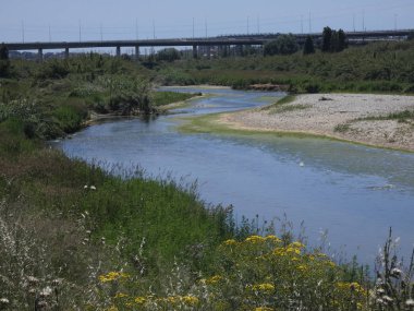 Rio baharda bir köprüyü geçerken, yansımaları ile mavi su gökyüzünün yansıması nedeniyle. Llobregat Nehri, Sant Feliu de Llobregat'tan geçerken Akdeniz'in ağzına çok yakın