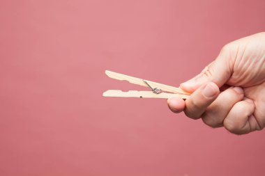 Elbise mandalları, renkli arka planda yetişkin bir elin parmaklarında ahşap clothespins.