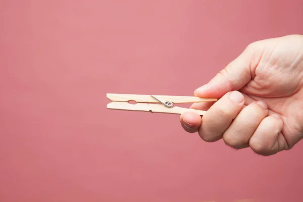 Clothes pegs, wooden clothespins on the fingers of an adult hand on color background.