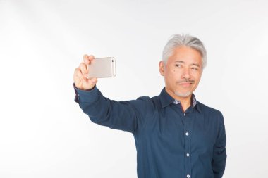 Elinde akıllı telefon olan orta yaşlı bir adam iletişim kuruyor ve selfie çekiyor. Telefonuyla fotoğraf çeken bir adam.