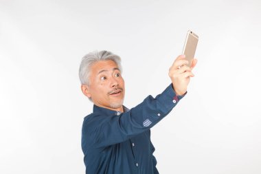 Elinde akıllı telefon olan orta yaşlı bir adam iletişim kuruyor ve selfie çekiyor. Telefonuyla fotoğraf çeken bir adam.