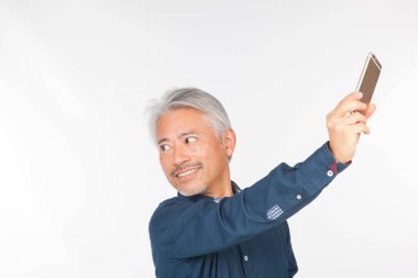 Elinde akıllı telefon olan orta yaşlı bir adam iletişim kuruyor ve selfie çekiyor. Telefonuyla fotoğraf çeken bir adam.