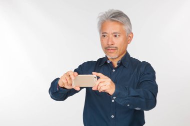 Elinde akıllı telefon olan orta yaşlı bir adam iletişim kuruyor ve selfie çekiyor. Telefonuyla fotoğraf çeken bir adam.