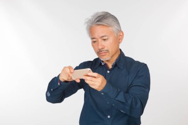 Elinde akıllı telefon olan orta yaşlı bir adam iletişim kuruyor ve selfie çekiyor. Telefonuyla fotoğraf çeken bir adam.