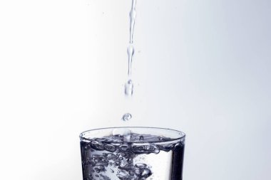Temiz, içme suyu temiz bir bardağa dökülüyor, sağlıklı, sağlıklı, temiz, kokusuz ve tatsız bir su. Yüzeye su damlaları sıçrıyor. Jet su bardağa giriyor