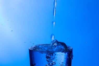 Temiz, içme suyu temiz bir bardağa dökülüyor, sağlıklı, sağlıklı, temiz, kokusuz ve tatsız bir su. Yüzeye su damlaları sıçrıyor. Jet su bardağa giriyor