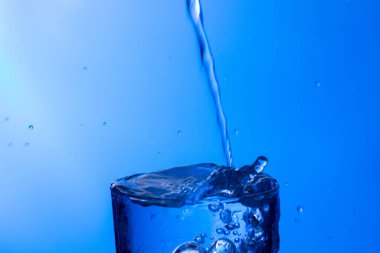 Temiz, içme suyu temiz bir bardağa dökülüyor, sağlıklı, sağlıklı, temiz, kokusuz ve tatsız bir su. Yüzeye su damlaları sıçrıyor. Jet su bardağa giriyor