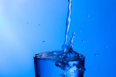 Temiz, içme suyu temiz bir bardağa dökülüyor, sağlıklı, sağlıklı, temiz, kokusuz ve tatsız bir su. Yüzeye su damlaları sıçrıyor. Jet su bardağa giriyor