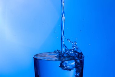 Temiz, içme suyu temiz bir bardağa dökülüyor, sağlıklı, sağlıklı, temiz, kokusuz ve tatsız bir su. Yüzeye su damlaları sıçrıyor. Jet su bardağa giriyor
