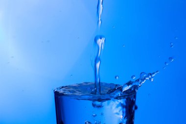 Temiz, içme suyu temiz bir bardağa dökülüyor, sağlıklı, sağlıklı, temiz, kokusuz ve tatsız bir su. Yüzeye su damlaları sıçrıyor. Jet su bardağa giriyor